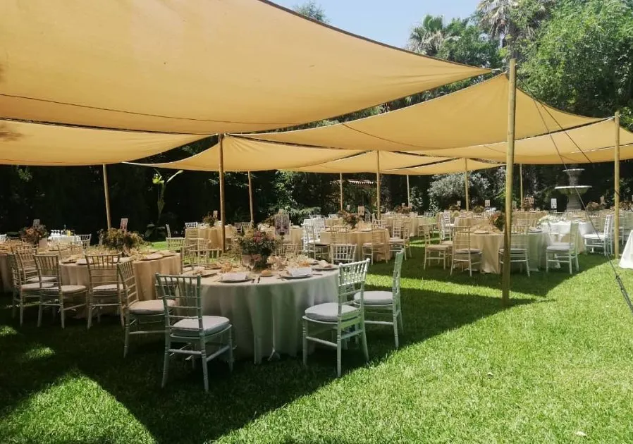 Mesas bajo toldos de lona en el césped, montadas para una comida